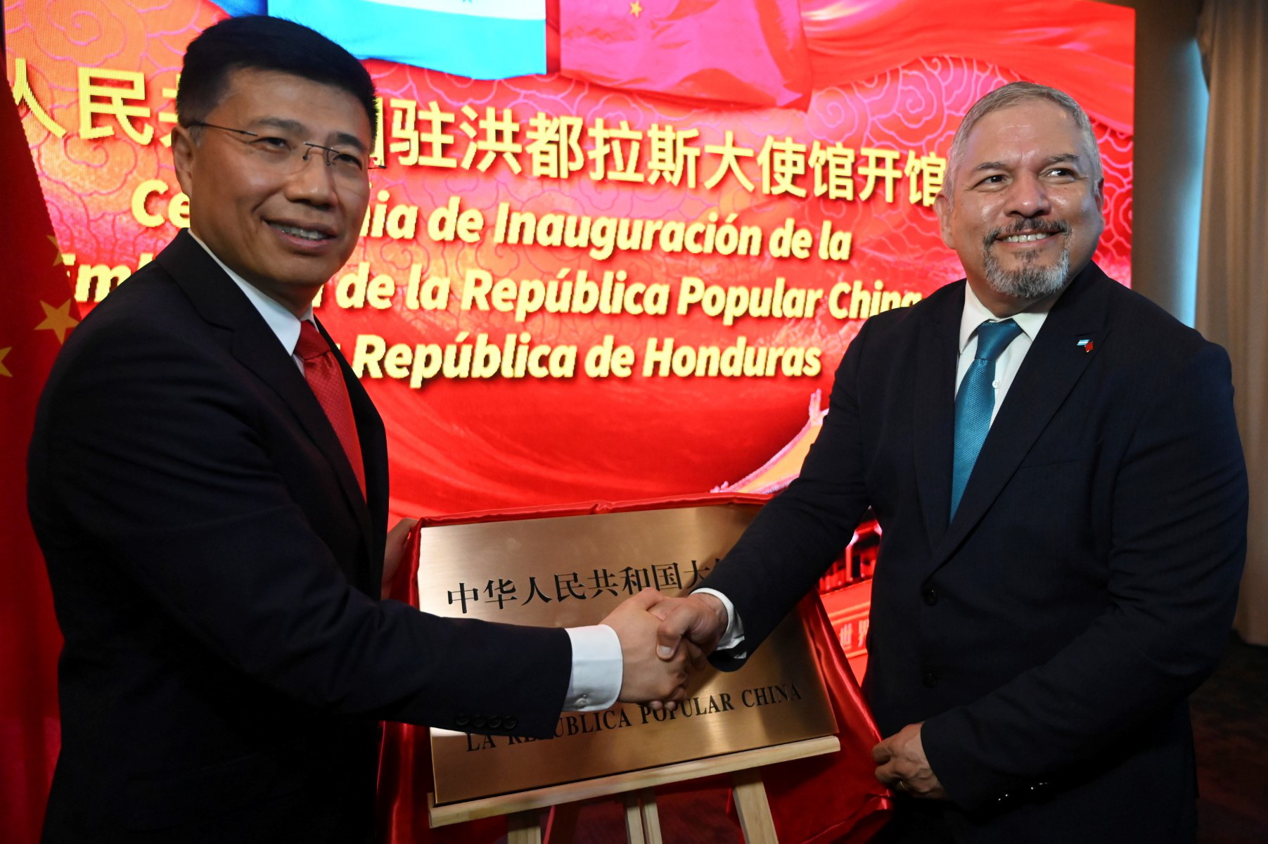 Eduardo Enrique Reina รัฐมนตรีต่างประเทศฮอนดูรัส (ขวา) และ Yu Bo จับมือกันระหว่างพิธีเปิดสถานทูตจีนในกรุงเตกูซิกัลปาเมื่อวันที่ 5 มิถุนายน - รูปภาพ: AFP