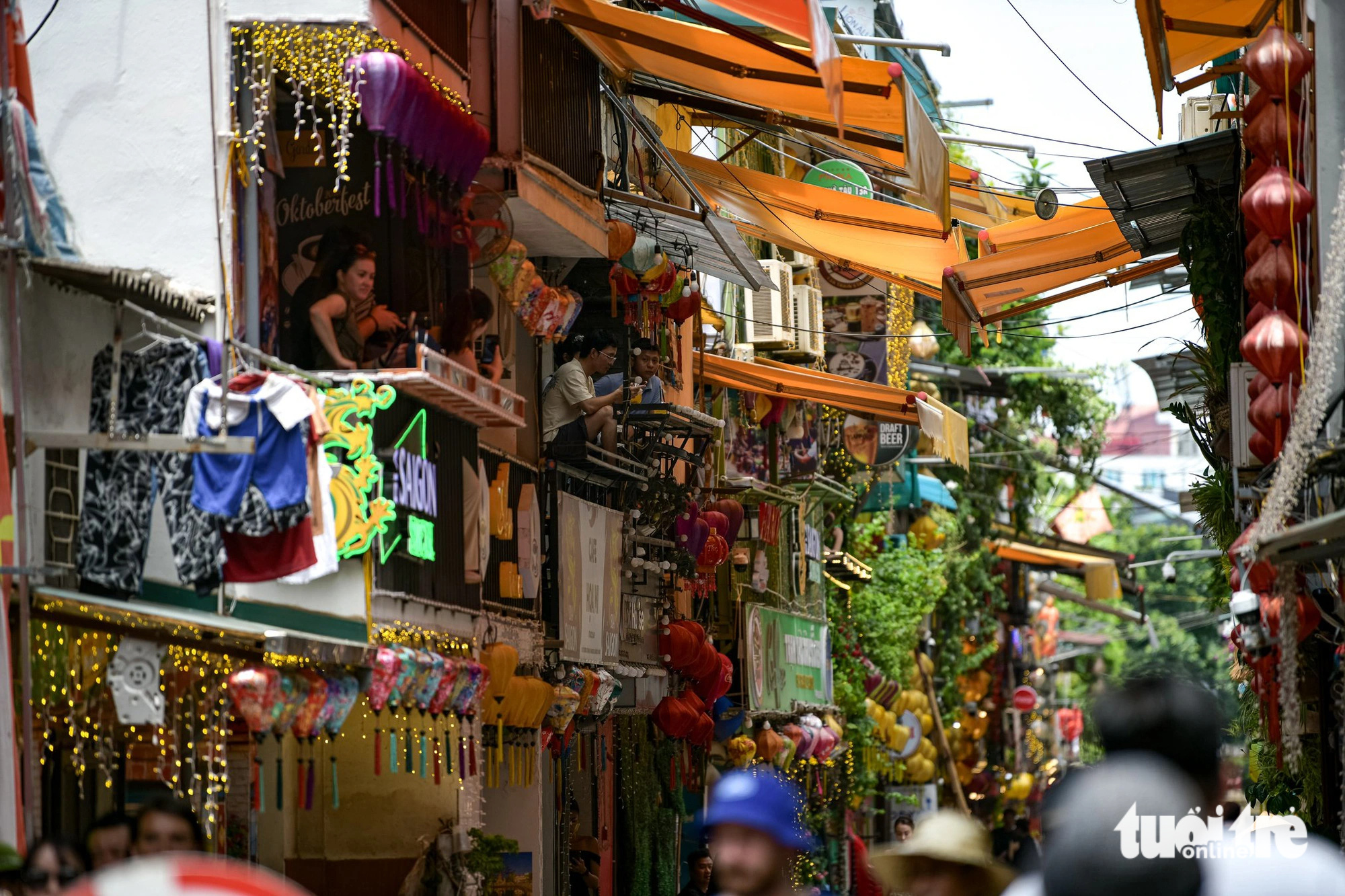 पर्यटक हनोई के मध्य में रेल की पटरियों को निहारते हुए कॉफी शॉप की दूसरी मंजिल पर बैठकर पेय का आनंद ले रहे हैं - फोटो: नाम ट्रान Du khách ngồi trên tầng 2 các quán cà phê, vừa thưởng thức đồ uống, vừa chiêm ngưỡng đường tàu giữa lòng Hà Nội - Ảnh: NAM TRẦN