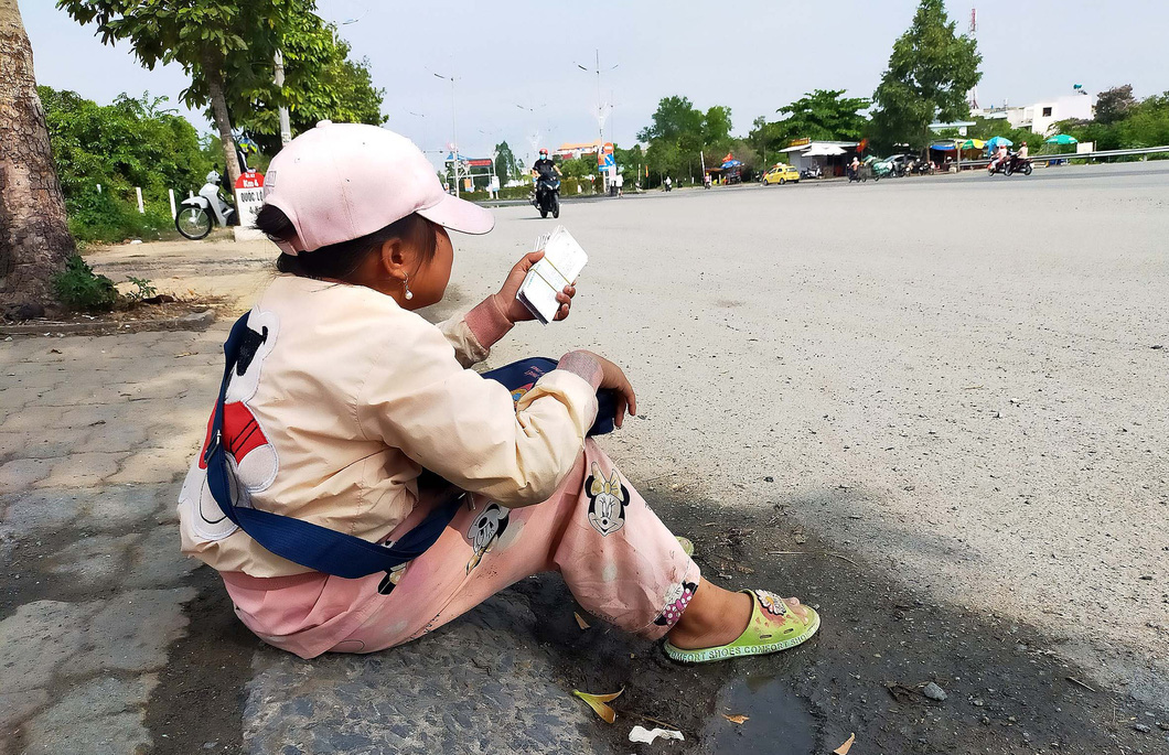 Bé Yến Nhi (11 tuổi, Long An) năn nỉ người qua đường mua vé số vì đã qua giờ trả vé nhưng vẫn còn 80 tờ chưa bán hết - Ảnh: M.TRƯỜNG