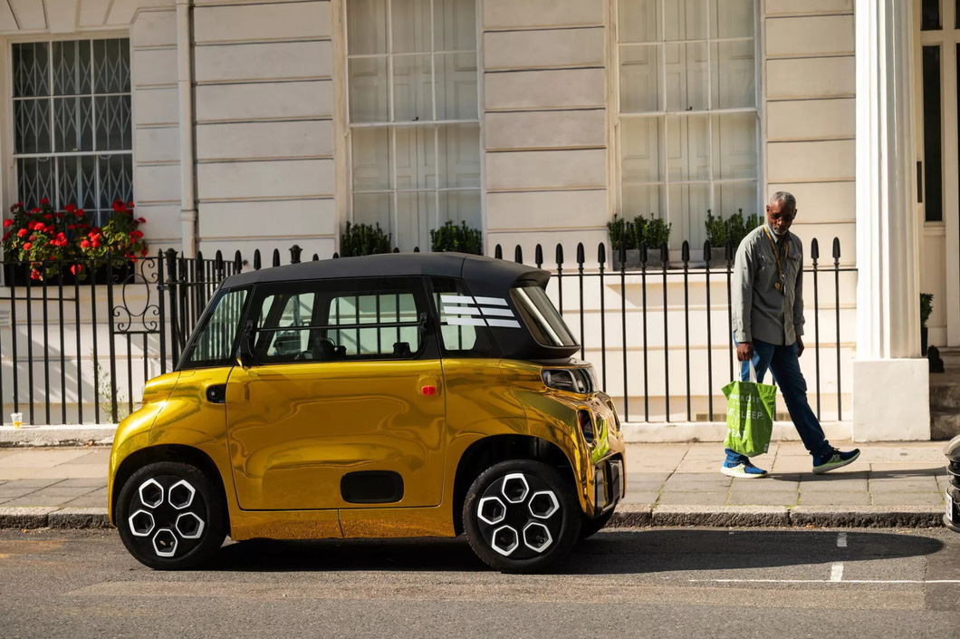 Electric mini car painted so brightly it looks like it's covered in gold, standing next to a supercar 