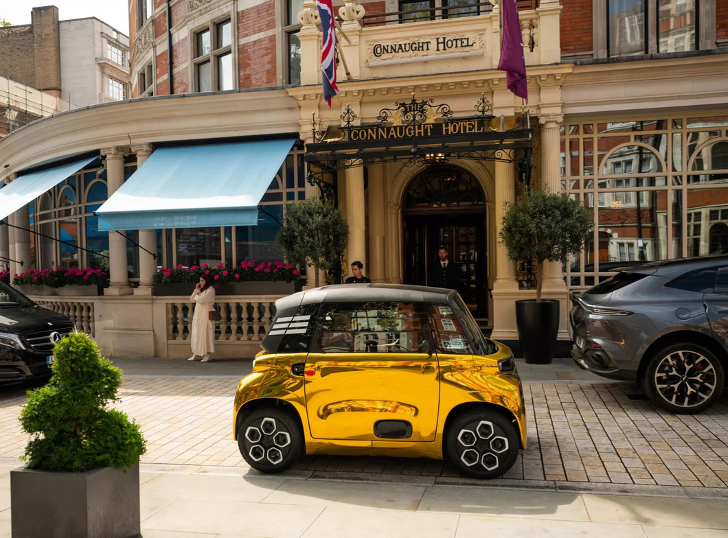 Electric mini car brightly painted as if covered in gold, parked next to supercar 