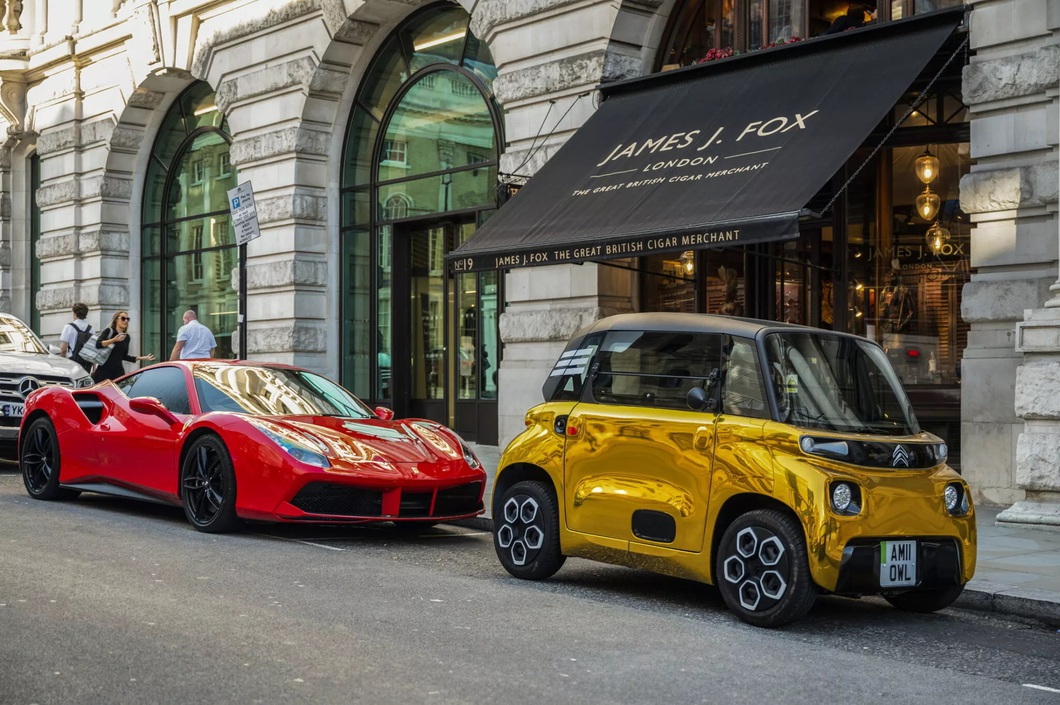 Mini electric car painted so brightly it looks like it's covered in gold, standing next to a supercar Mini electric car painted so brightly it looks like it's covered in gold, standing next to a supercar