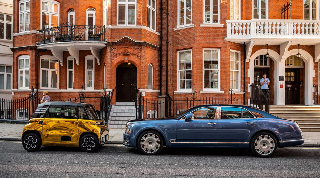 Electric mini car brightly painted as if covered in gold, parked next to supercar 