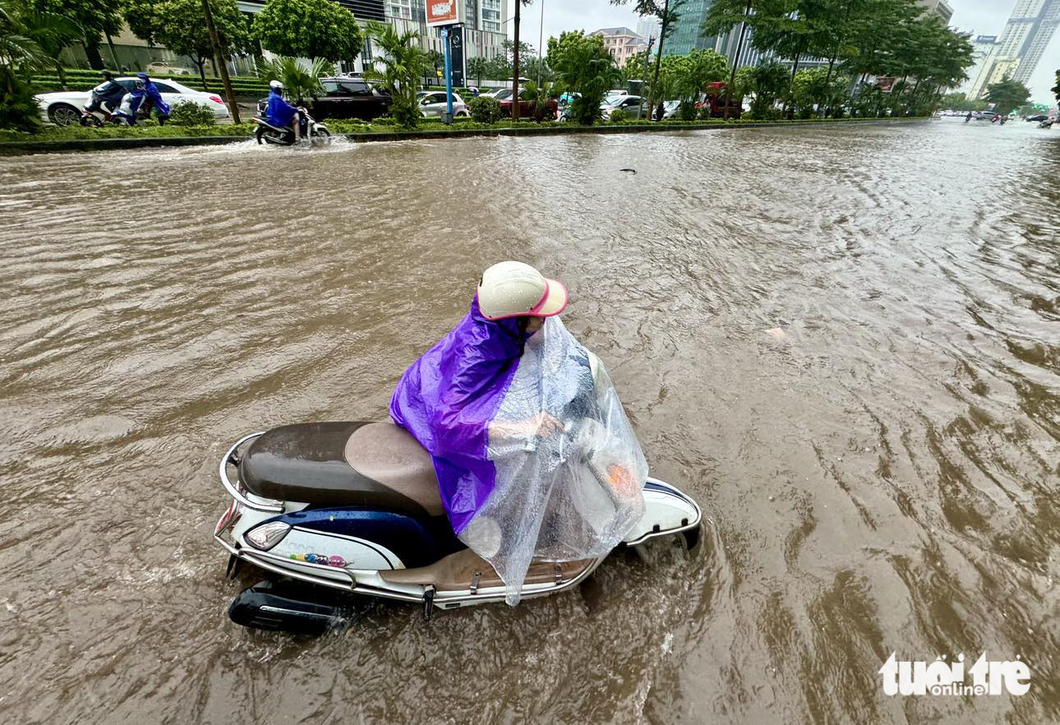 Một phụ nữ vất vả đẩy chiếc xe bị chết máy giữa khu vực bị ngập tại nút giao Dương Đình Nghệ - Phạm Hùng - Ảnh: NGUYỄN KHÁNH