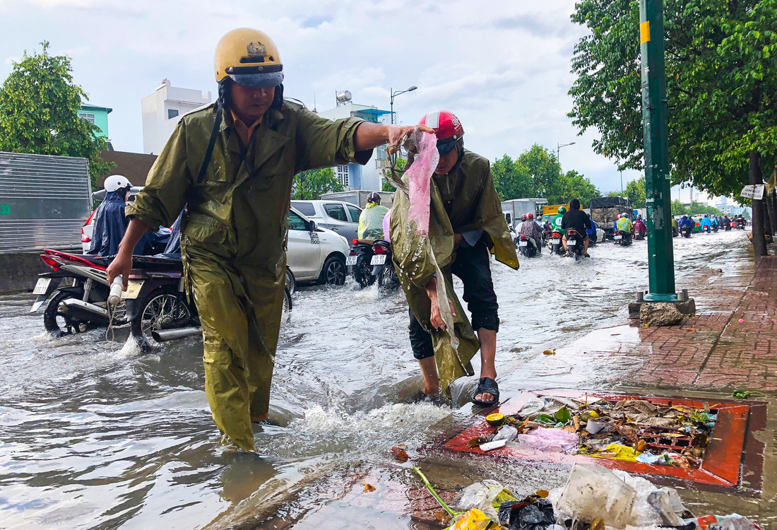 Đường Phạm Văn Đồng ngập, kẹt xe sau mưa lớn, CSGT phải moi rác cho nước chảy - Ảnh 1.