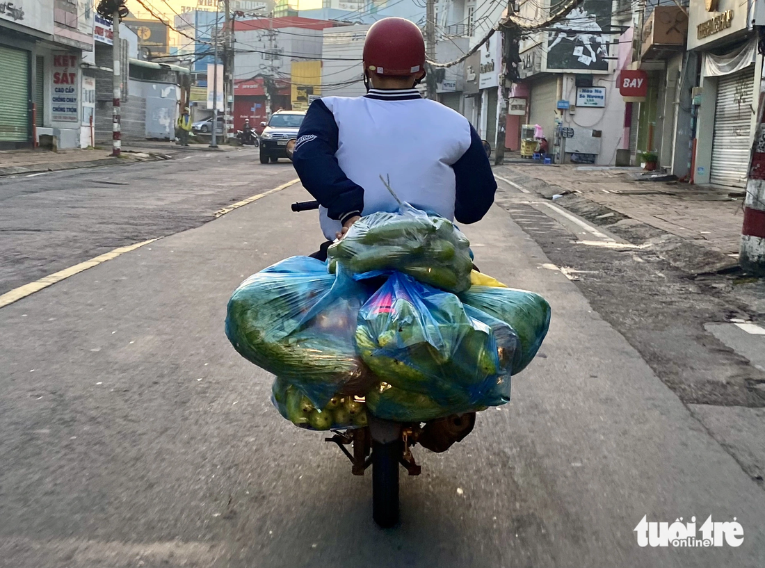 Chiếc xe thồ rau củ với nhiều bao bì móc sau xe trên đường Võ Văn Ngân