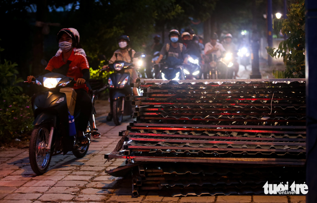 Người đi xe máy chạy sát hàng rào tôn sắt chất trên vỉa hè tiềm ẩn nguy cơ mất an toàn giao thông.