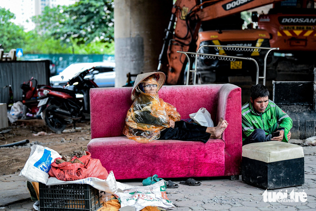 Một bà cụ bán bánh gai co ro trong chiếc áo mưa mỏng dưới gầm cầu vượt Mễ Trì, người chạy xe ôm núp sau chiếc sofa cũ tránh những cơn gió lạnh - Ảnh: NAM TRẦN