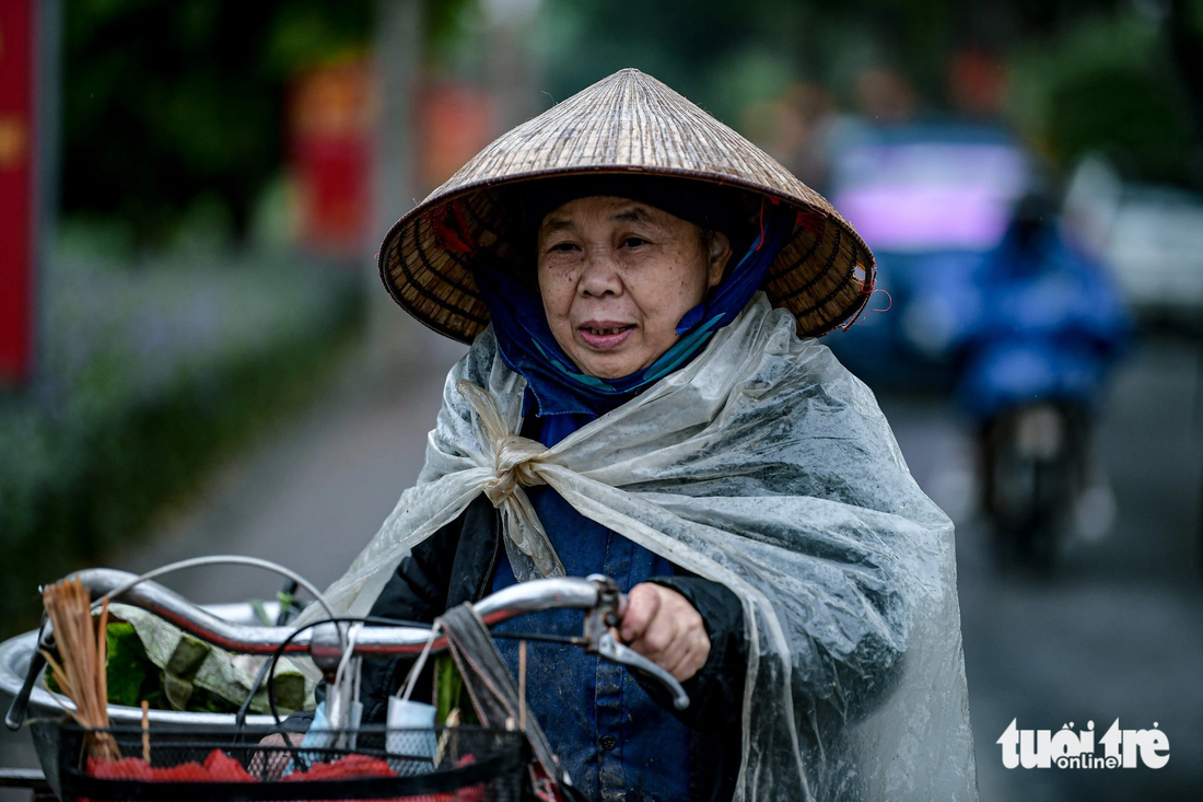 Cắt rau để đi bán từ sáng sớm, bà Tý (70 tuổi) cho biết hôm nay phải mặc ấm hơn. Ngoài áo, bà còn mặc 2 áo mưa để tránh mưa và lạnh - Ảnh: NAM TRẦN