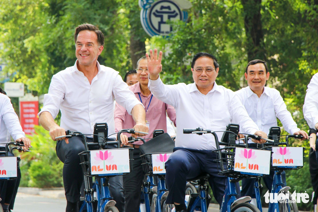 Thủ tướng Phạm Minh Chính và Thủ tướng Hà Lan Mark Rutte vẫy tay chào người đi bộ khi đạp xe trên đường Điện Biên Phủ - Ảnh: DUY LINH