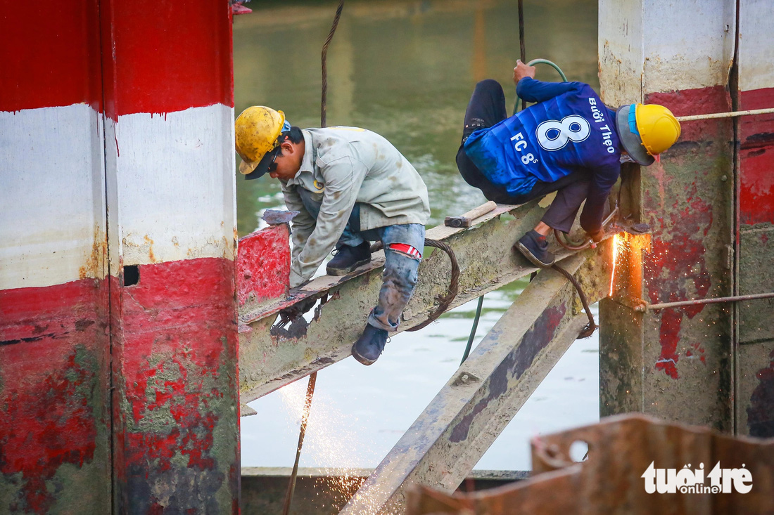 Các công nhân đang cắt các thanh sắt của trụ chống va đập của cầu cũ - Ảnh: CHÂU TUẤN