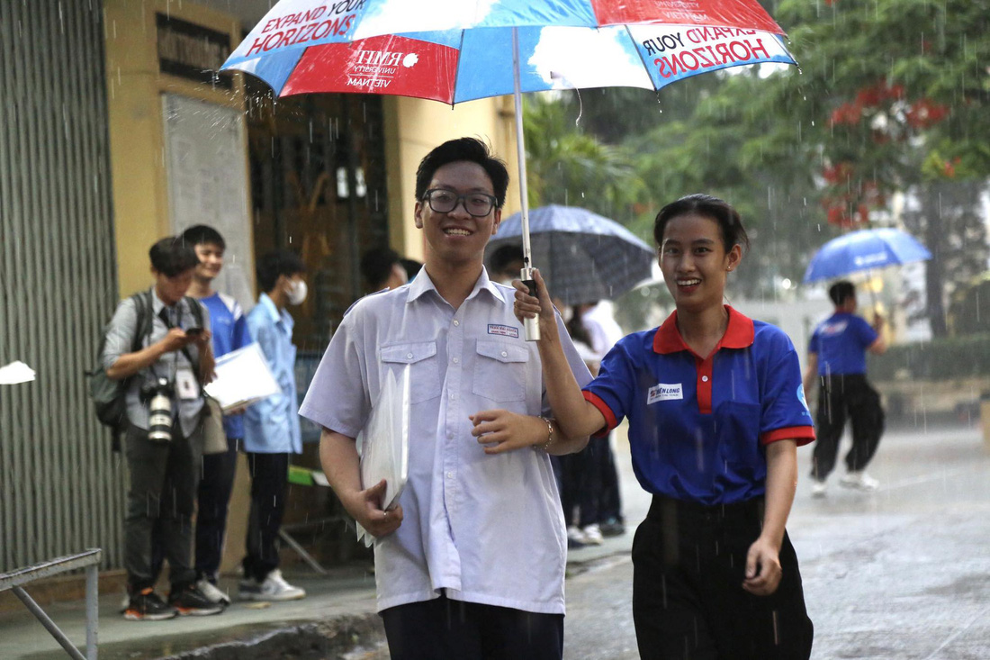 Thí sinh tại điểm thi THPT chuyên Trần Đại Nghĩa được tình nguyện viên hỗ trợ ra về trong cơn mưa lớn chiều 28-6 - Ảnh: PHƯƠNG QUYÊN