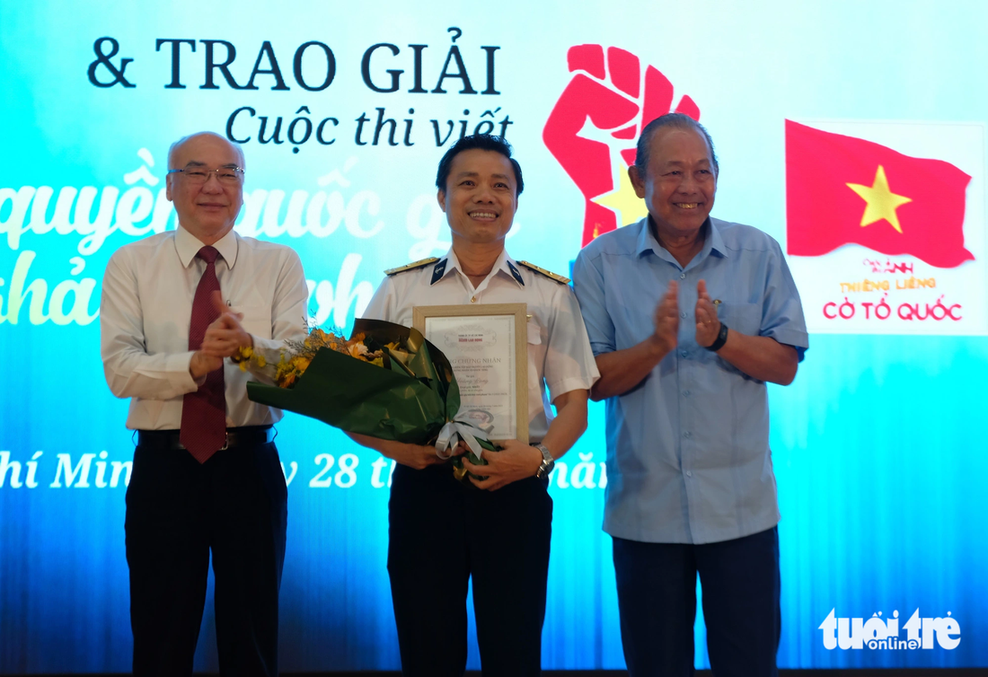 Ông Phan Nguyễn Như Khuê, trưởng Ban Tuyên giáo Thành ủy TP.HCM (bìa trái) và ông Trương Hòa Bình, nguyên phó thủ tướng thường trực (bìa phải), trao giải nhất cuộc thi viết Chủ quyền quốc gia bất khả xâm phạm cho tác giả Hoàng Long (Mai Thắng) - Ảnh: LINH ĐOAN