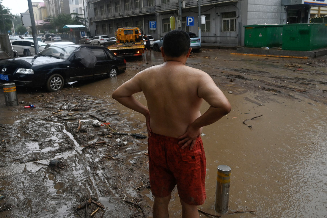Một cư dân đứng trước hiện trường xe hơi hư hỏng sau cơn mưa kéo dài tại Bắc Kinh - Ảnh: AFP