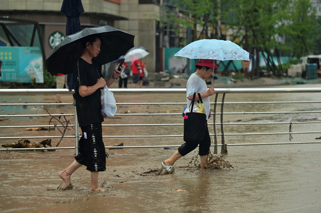 Người dân đi trên đường phố ngập nước tại quận Môn Đầu Câu, Bắc Kinh - Ảnh: AFP