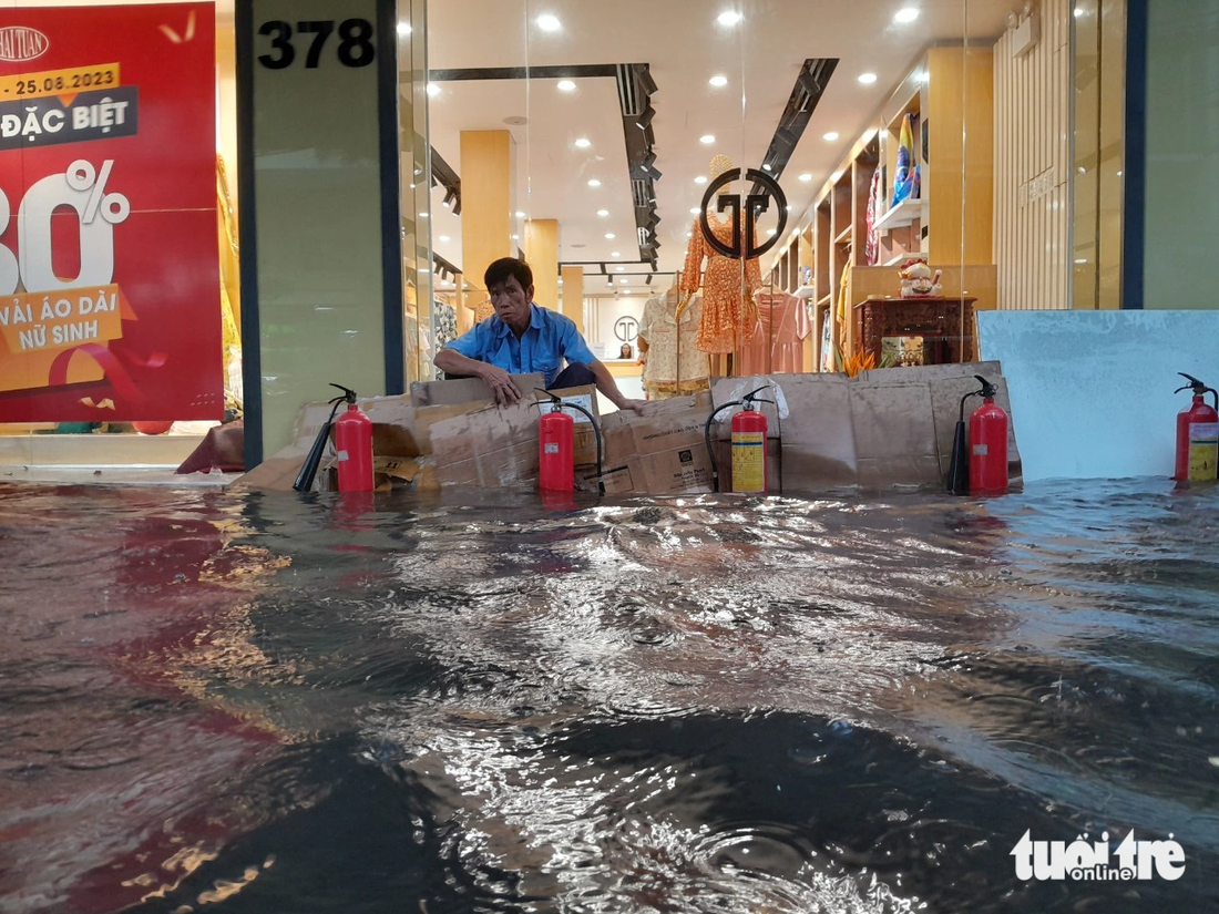 Một cửa hàng kinh doanh trên đường Hà Hoàng Hổ, TP Long Xuyên phải dùng bình chữa cháy, bìa các tông để chắn nước, rác do ngập nặng - Ảnh: CHÍ HẠNH