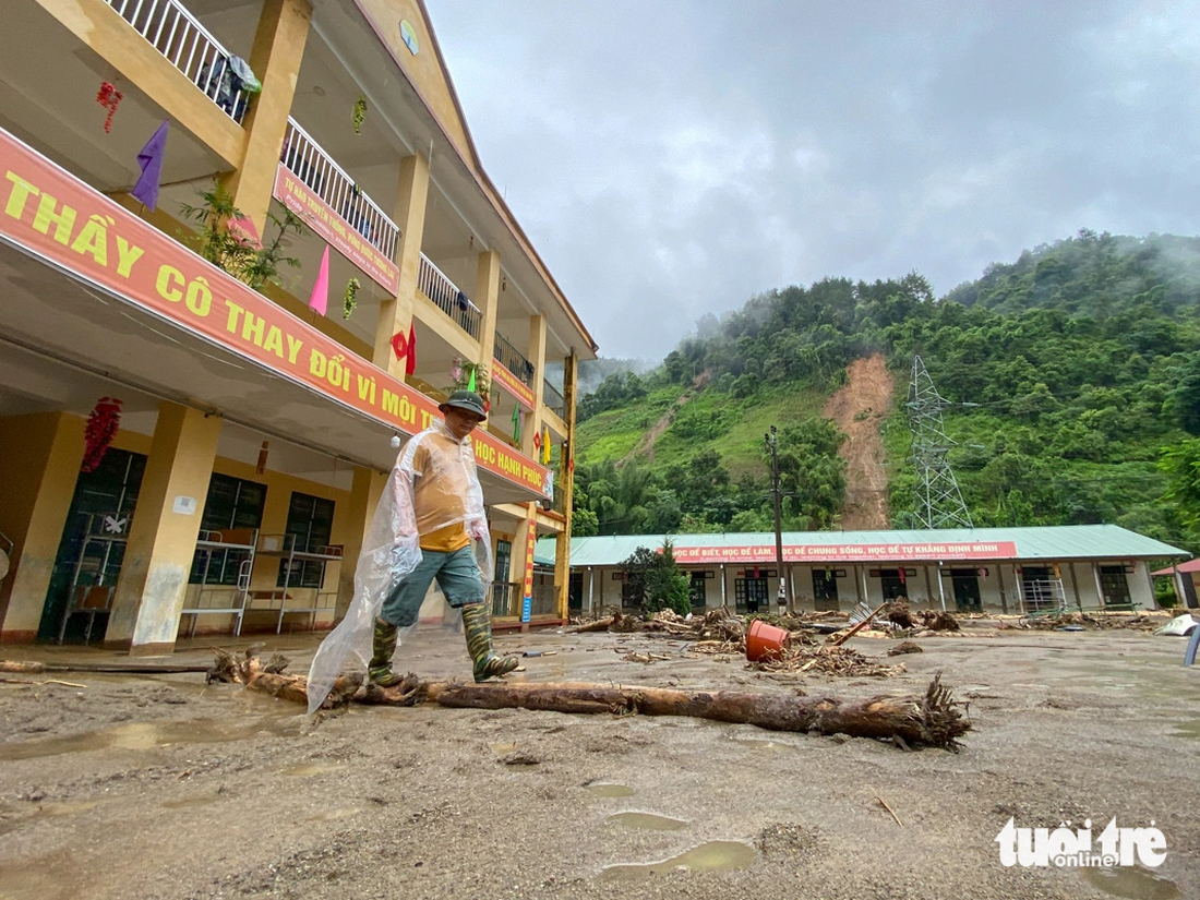 Thầy Nguyễn Xuân Trường - hiệu trưởng Trường phổ thông dân tộc bán trú tiểu học và THCS Hồ Bốn - phải đặt các thân cây gỗ để đi vào lớp học do khuôn viên trường ngập bùn đất - Ảnh: CHÍ TUỆ