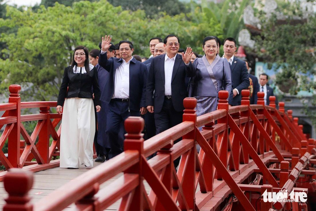 Thủ tướng Phạm Minh Chính cùng phu nhân, Thủ tướng Lào Sonexay Siphandone và phu nhân vẫy tay chào người dân khi đi qua cầu Thê Húc dẫn vào đền Ngọc Sơn - Ảnh: NGUYỄN KHÁNH