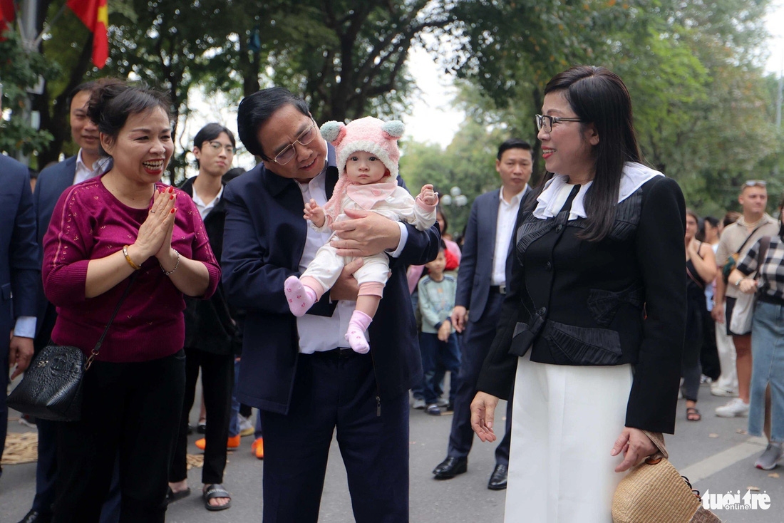 Thủ tướng Phạm Minh Chính và phu nhân bế một em bé được gia đình đưa đi chơi ở hồ Gươm trong lúc chờ Thủ tướng Lào và phu nhân đến điểm hẹn - Ảnh: NGUYỄN KHÁNH