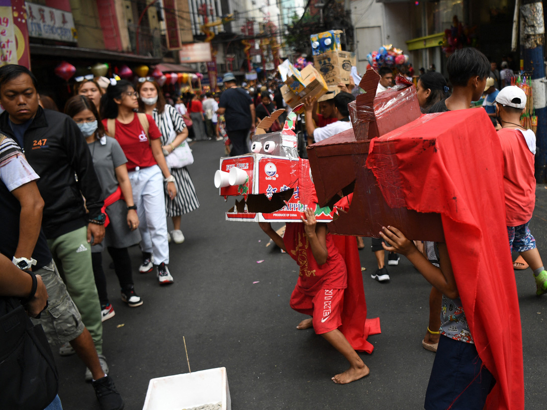 Trẻ em vui đùa cùng những chú lân giả tự chế từ bìa các tông trên đường phố Manila sáng đầu năm - Ảnh: AFP