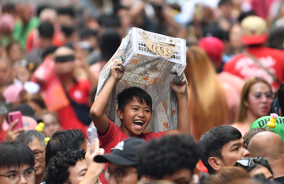 Bé trai ở Manila vui đùa bên chú lân giả làm từ khay nhựa - Ảnh: AFP