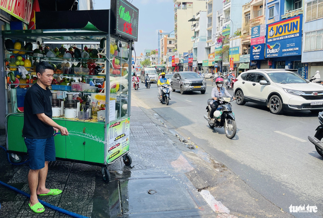Anh Sơn, ngụ đường Bạch Đằng, quận Bình Thạnh, tưới nước lên mặt đường để giảm bớt cái nóng hắc lên - Ảnh: LÊ PHAN