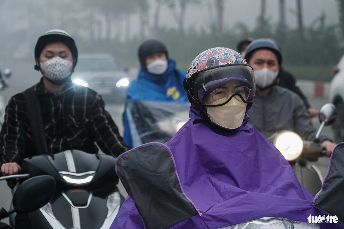 Nhiều người Hà Nội phải mặc thêm áo mưa dù trời không mưa, do quá nhiều sương mù - Ảnh: PHẠM TUẤN