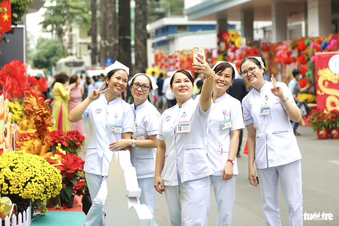 Các điều dưỡng, y tá của bệnh viện tranh thủ ghé đường hoa chụp ảnh lưu niệm trước khi vào ca trực - Ảnh: PHƯƠNG QUYÊN