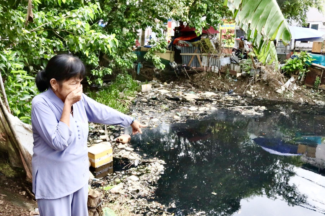 Bà Trần Thị Chín (65 tuổi, phường Hiệp Bình Chánh, TP Thủ Đức) lấy tay bịt mũi chỉ phóng viên khu vực rác thải tồn đọng gây ô nhiễm tại rạch Cầu Làng - Ảnh: TIẾN QUỐC