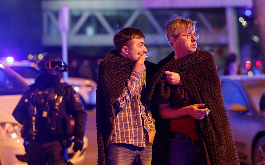 Hai người đàn ông cùng sưởi ấm sau khi thoát khỏi hiện trường vụ xả súng - Ảnh: REUTERS