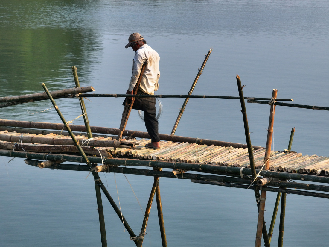 Một người thợ chống nạng đi trên mặt cầu mới lát bằng thân tre để buộc dây thép kết nối