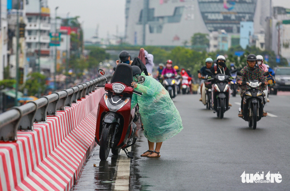 Mưa bất ngờ khiến một số người đi xe máy dừng mặc áo mưa ngay trên cầu vượt Bình Lợi - Ảnh: CHÂU TUẤN