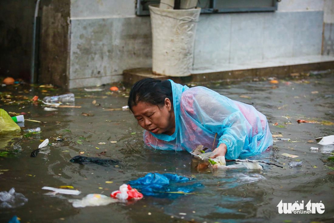 Do rác bịt kín các miệng cống nên người dân phải đội mưa đi móc cống - Ảnh: CHÂU TUẤN