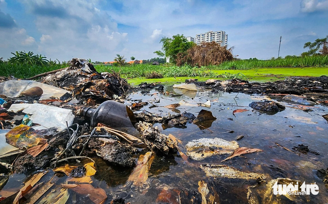Dưới đầm lầy, nhiều chai thủy tinh vỡ nát kèm với đủ loại rác thải đã cháy sém - Ảnh: CHÂU TUẤN