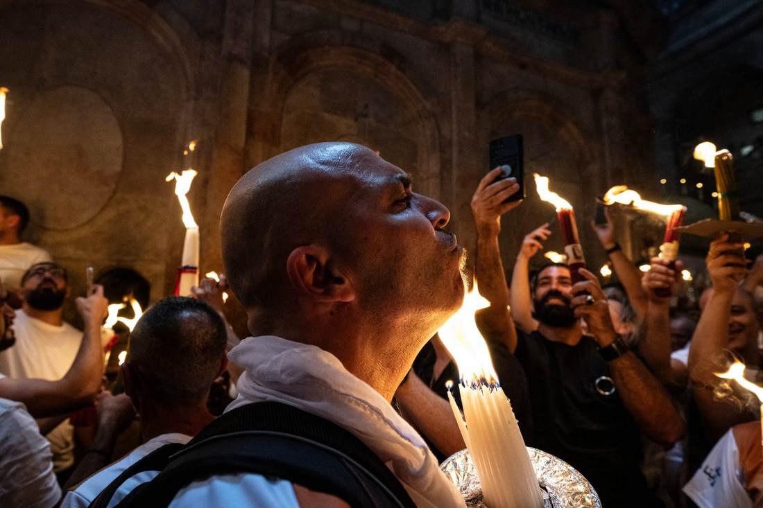Một tín đồ hơ ngọn lửa để nhận lấy phép lành từ lửa Phục sinh. Theo những người hành hương và những người thuộc hàng giáo phẩm của Chính Thống giáo, trong vòng 33 phút đầu tiên sau khi được lấy ra từ "mộ Thánh", ngọn lửa không gây phỏng dù các tín đồ hơ qua cơ thể - Ảnh: AFP