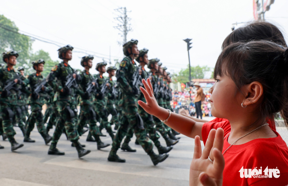 Một bé gái mặc áo hình cờ Tổ quốc vẫy tay chào khối chiến sĩ lục quân khi đi ngang qua một con phố tại Điện Biên - Ảnh NGUYỄN KHÁNH
