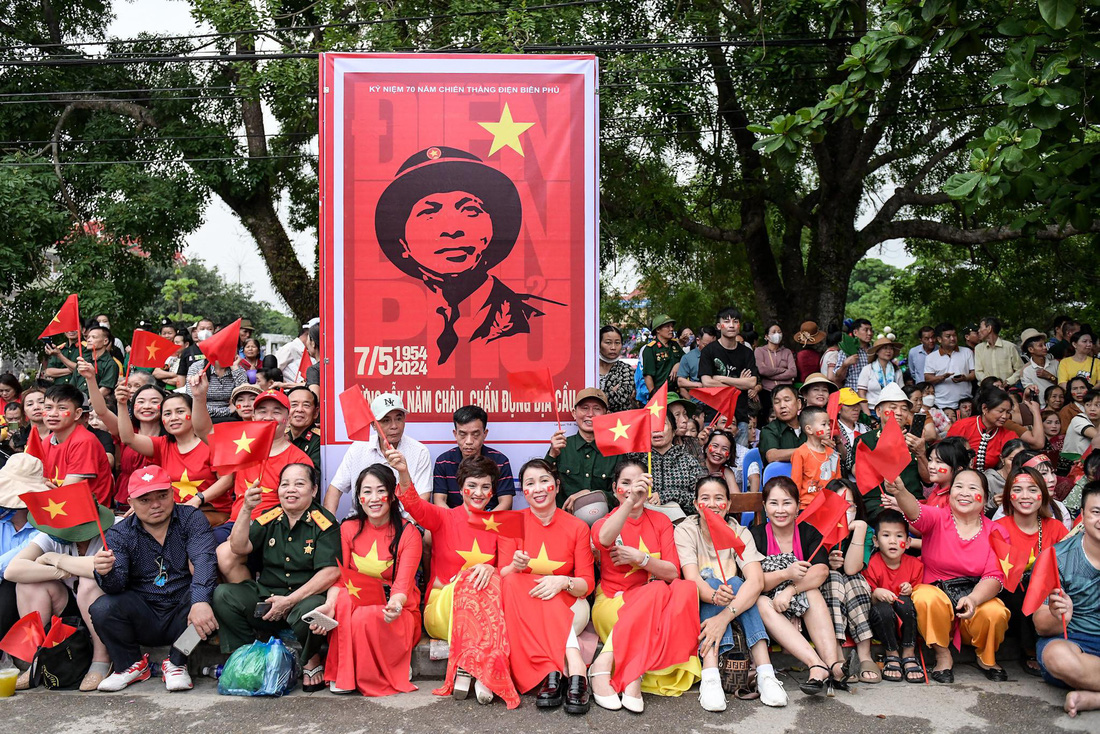 Người dân cầm cờ ngồi chờ khắp các ngả đường TP Điện Biên Phủ chờ đoàn diễu binh, diễu hành đi qua - Ảnh: NAM TRẦN