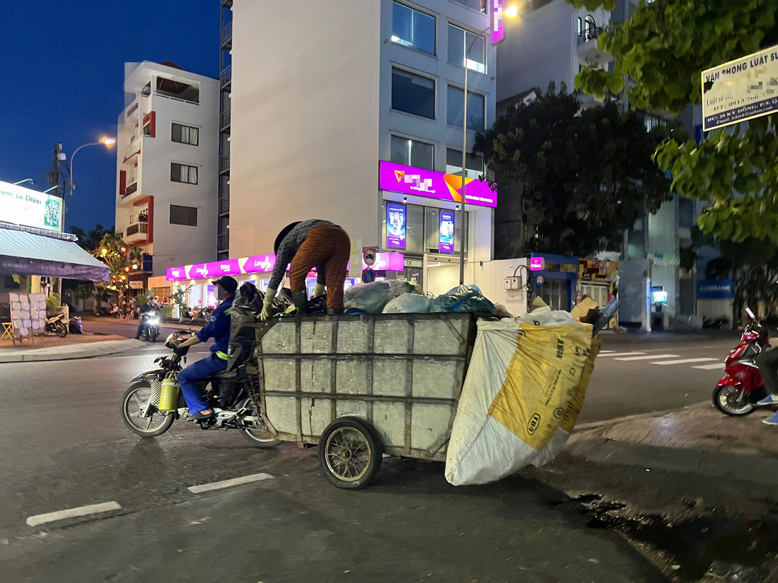 Xe vừa chạy trên đường, người phụ nữ vừa đứng trên thùng xe để ấn rác xuống dưới 