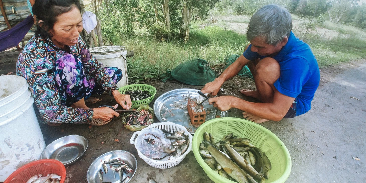 tranh thủ vắng khách, vợ chồng ông bảy tá làm cá bán ở chợ bên đường - ảnh quốc việt