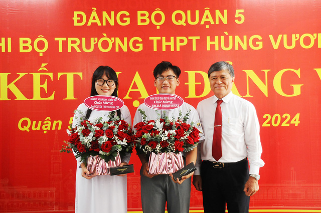 Thầy Nguyễn Văn Hiếu (giám đốc Sở GD&ĐT TP.HCM) trao hoa chúc mừng 2 bạn đảng viên mới. Ảnh:NGUYỄN HƯNG