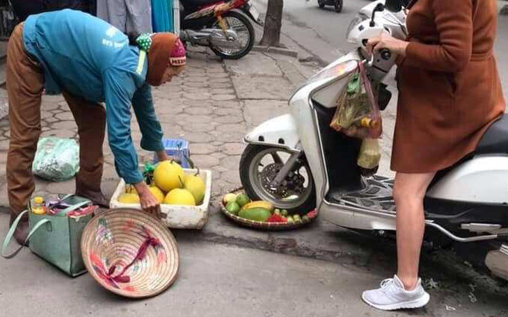 Người phụ nữ cán xe máy qua mẹt trái cây của chị bán hàng rong