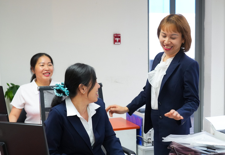 Chị Nguyễn Thị Thùy Trang (đứng), Đội phó Đội Dịch vụ khách hàng, Công ty Điện lực Tân Bình, EVNHCMC trao đổi công việc cùng nhân viên Tổ Giao dịch - Ảnh: HỮU HẠNH