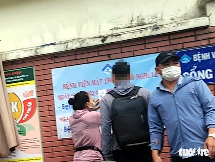 “Cò” Thủy (trái) và “cò” Lâm (đội nón) chào bán số thứ tự trước cổng Bệnh viện Mắt TP.HCM sáng 2-1-2023 - Ảnh cắt từ video