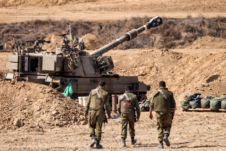 Một vài người lính Israel đi bộ gần khẩu pháo tự hành ở khu vực biên giới Gaza ngày 12-10 - Ảnh: AFP