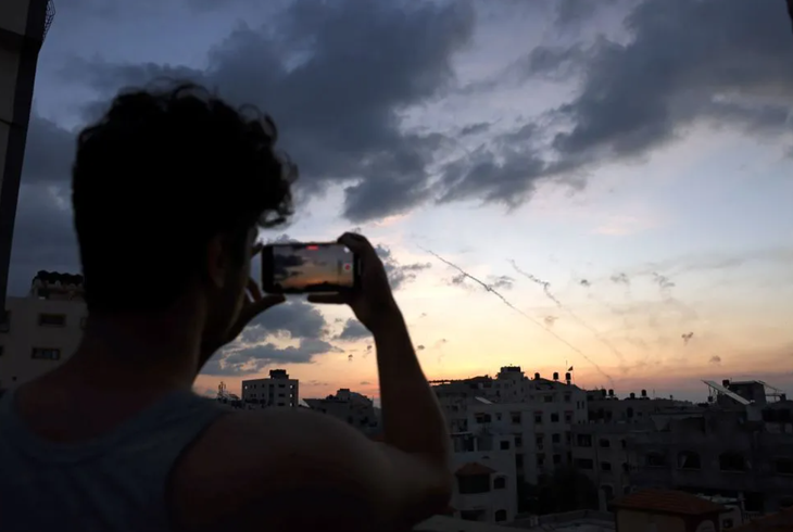 Một người đàn ông ghi lại hình ảnh không kích từ Dải Gaza vào Israel ngày 7-10 - Ảnh: AFP