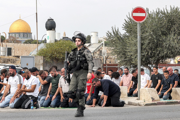 Một nữ quân nhân Israel đi ngang qua những tín đồ Hồi giáo đang cầu nguyện ở núi Ô-liu, đông Jerusalem ngày 27-10. Buổi cầu nguyện diễn ra trước các cuộc tuần hành thể hiện tình đoàn kết với người dân Palestine ở Dải Gaza - Ảnh: AFP