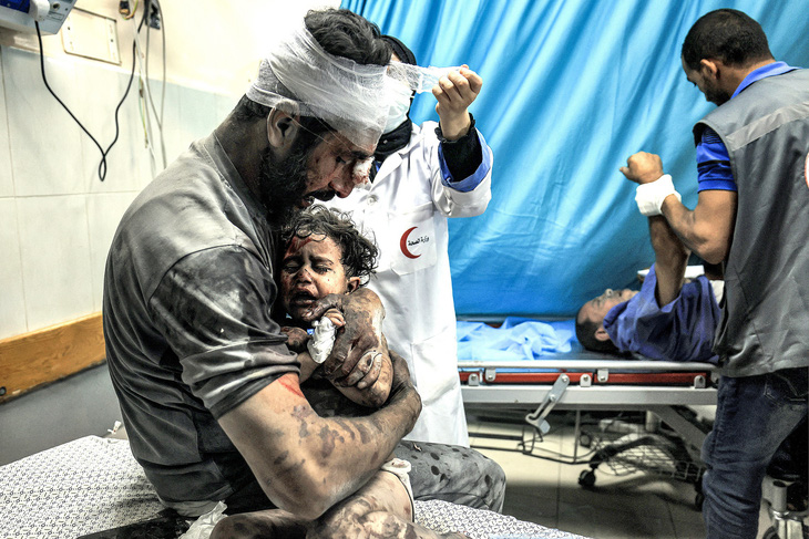 Người đàn ông bị thương ôm chặt đứa bé đang la khóc tại một bệnh viện ở phía nam Dải Gaza vào ngày 24-10 - Ảnh: AFP