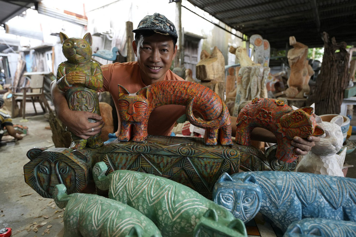 Nghệ nhân Lê Ngọc Thuận, chủ xưởng mộc nghệ thuật Làng Củi Lũ, với bộ sưu tập mèo gỗ làm từ gỗ mục - Ảnh: B.D.