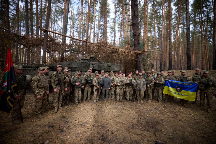 Binh sĩ Ukraine chụp ảnh chung với Tổng thống Volodymyr Zelensky khi ông đến thăm các đơn vị tiền tuyến - Ảnh: REUTERS