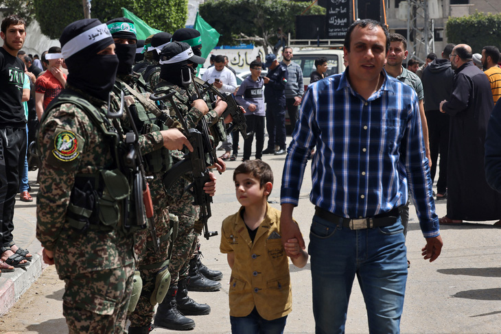 Một người đàn ông Palestine cùng con trai đi ngang qua các thành viên của Hamas ở thành phố Jabalia, phía Bắc dải Gaza, ngày 7-4 - Ảnh: AFP